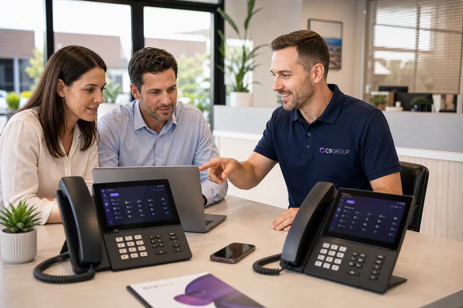 C9 GROUP consultant in navy polo helping a growing team plan call routing with desk phones and laptop dashboard