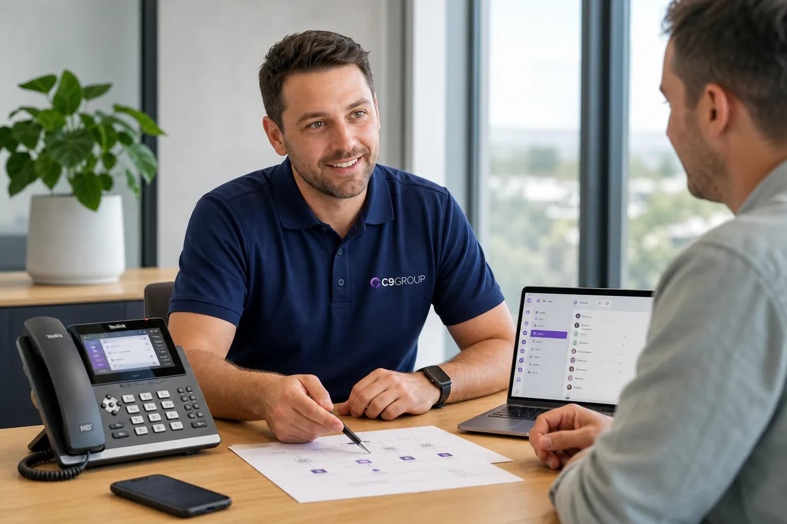 C9 GROUP consultant in navy polo helping configure VoIP phone services with Yealink handset and softphone