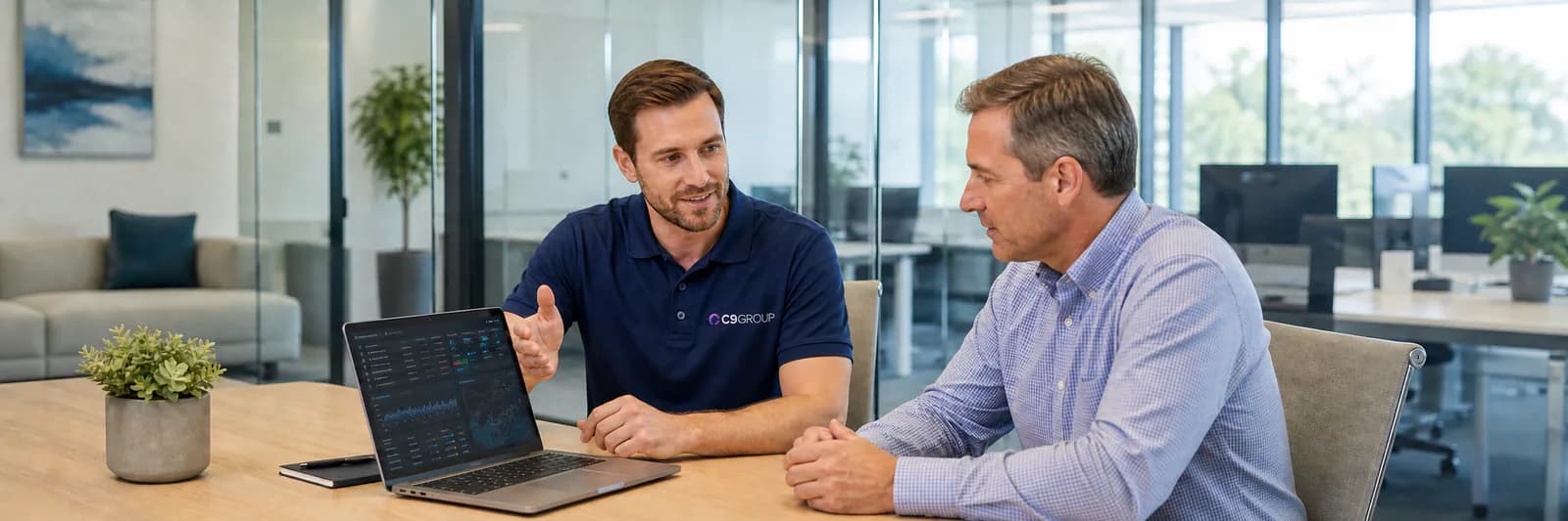 C9 GROUP staff member in navy polo explaining network security to a business owner on a laptop